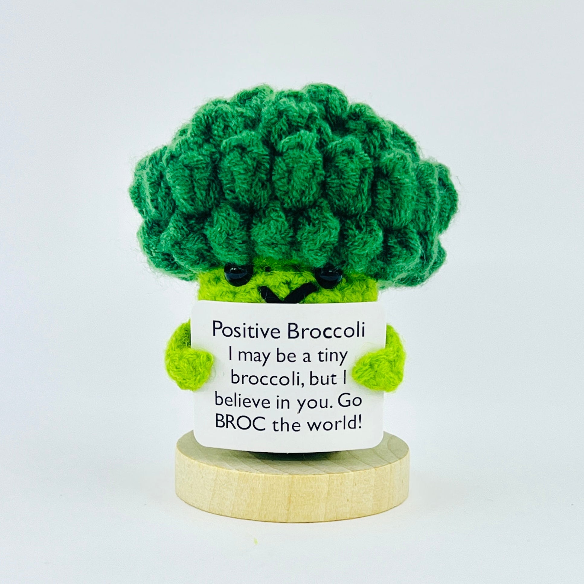 Green crochet broccoli with a white tag on a light gray background